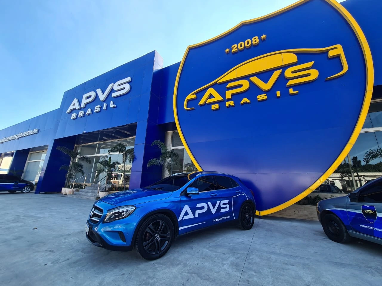 Fachada da sede da APVS Brasil, com o escudo gigante da associação e veículos adesivados da frota
